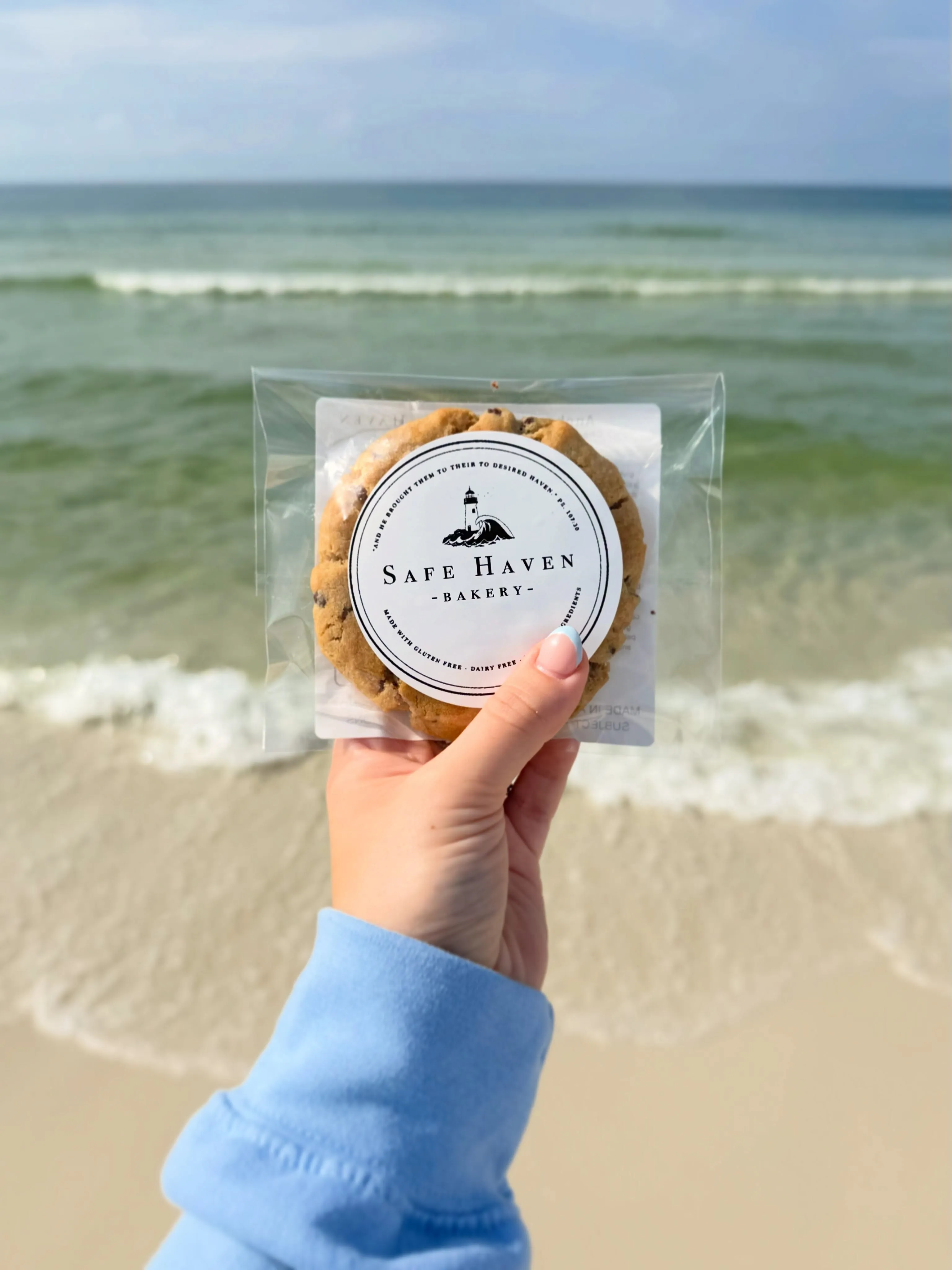 A Safe Haven cookie in its labelled bag, held up against the ocean