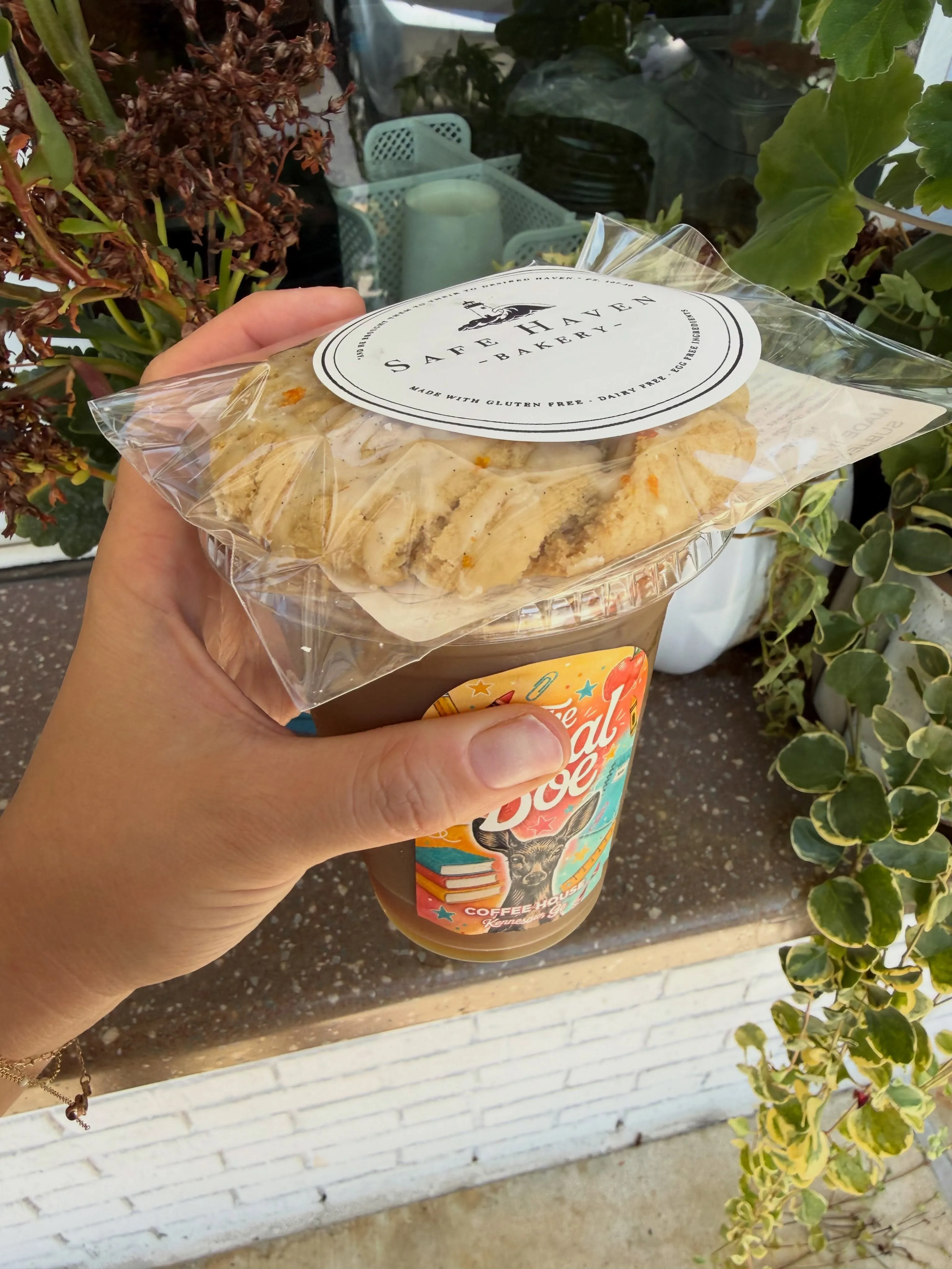 A Safe Haven cookie in its labelled bag, resting on an iced coffee from The Local Doe