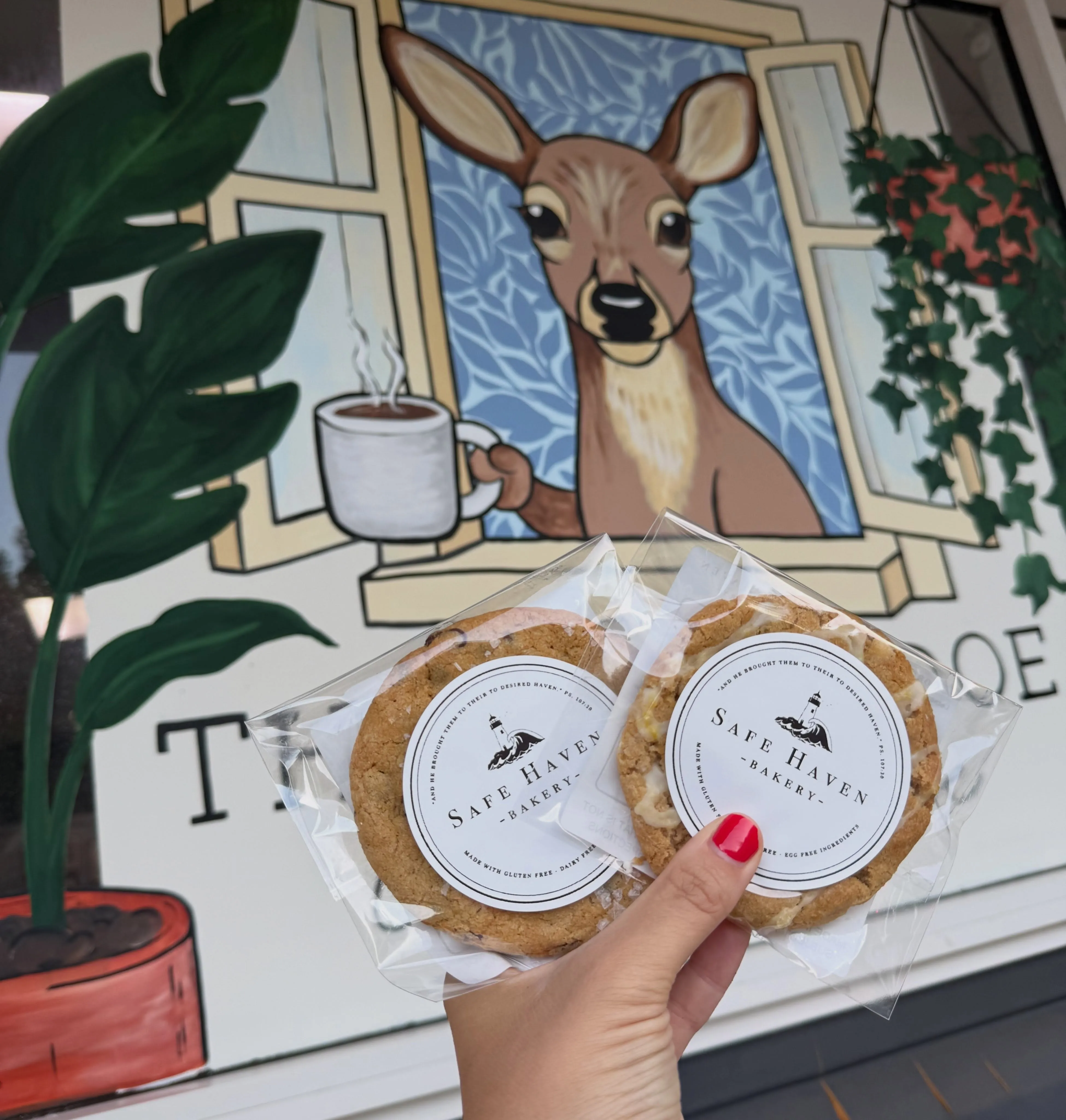 Two Safe Haven cookies held up in front of The Local Doe’s painted deer mural
